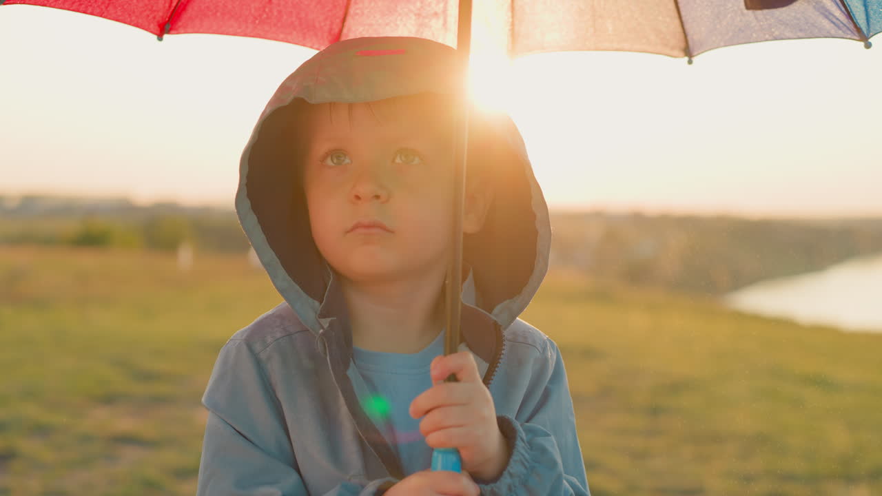 우산 에 숨어있는 상처받은 소년, 아이의 슬은 비와 혼합되는 것처럼 보입니다.