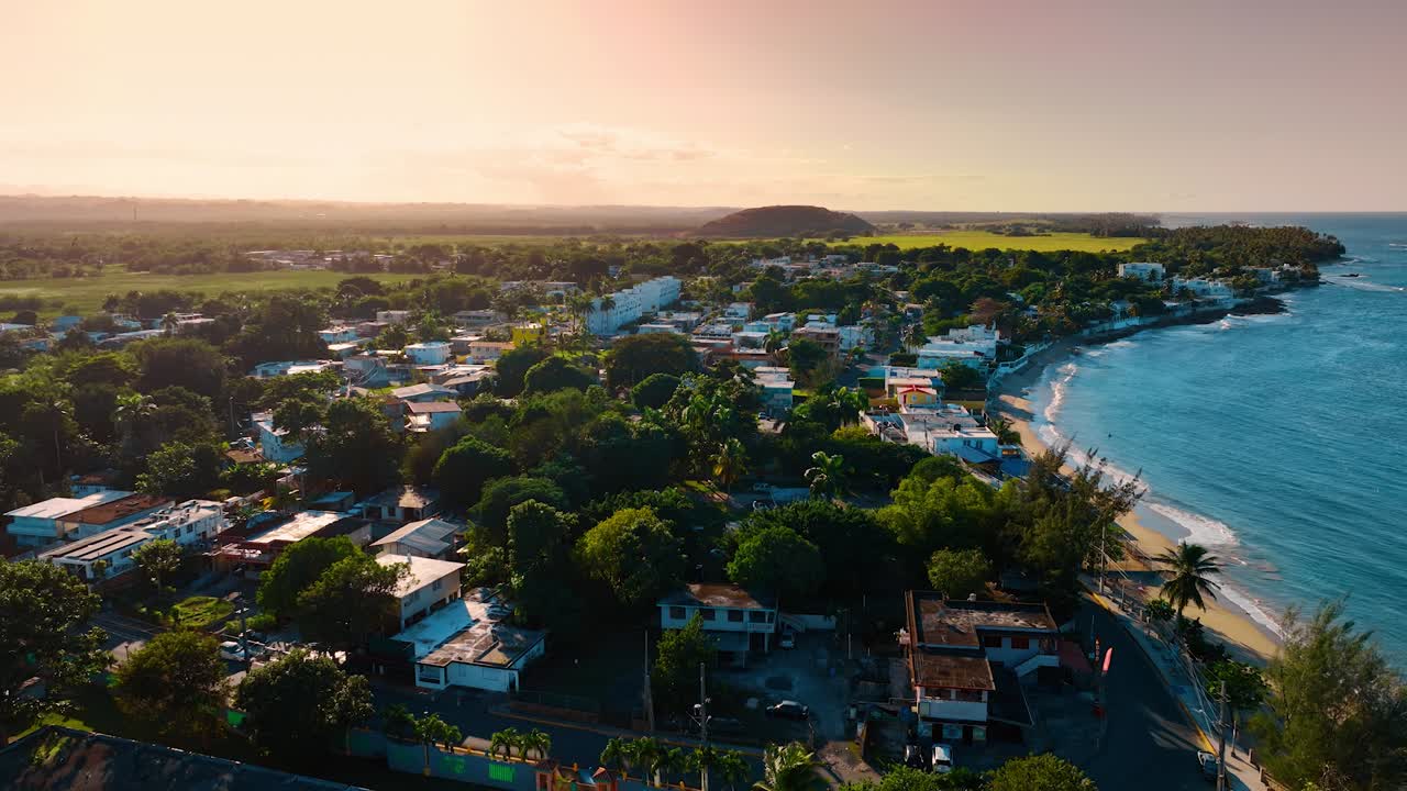 Cidade costeira e praia ao pôr do sol em Porto Rico. Vista aérea de uma vila à beira-mar com palmeiras e água azul-turquesa durante a luz quente do entardecer.