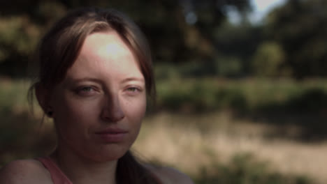 close up of a young woman's face under the shade of a tree with the sun's rays falling on it as she gazes to the side