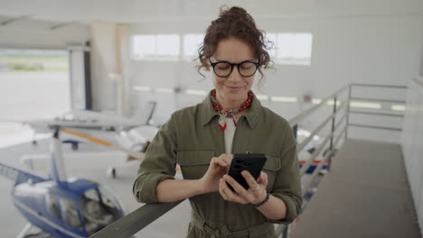female aircraft maintenance engineer texting on phone in hangar