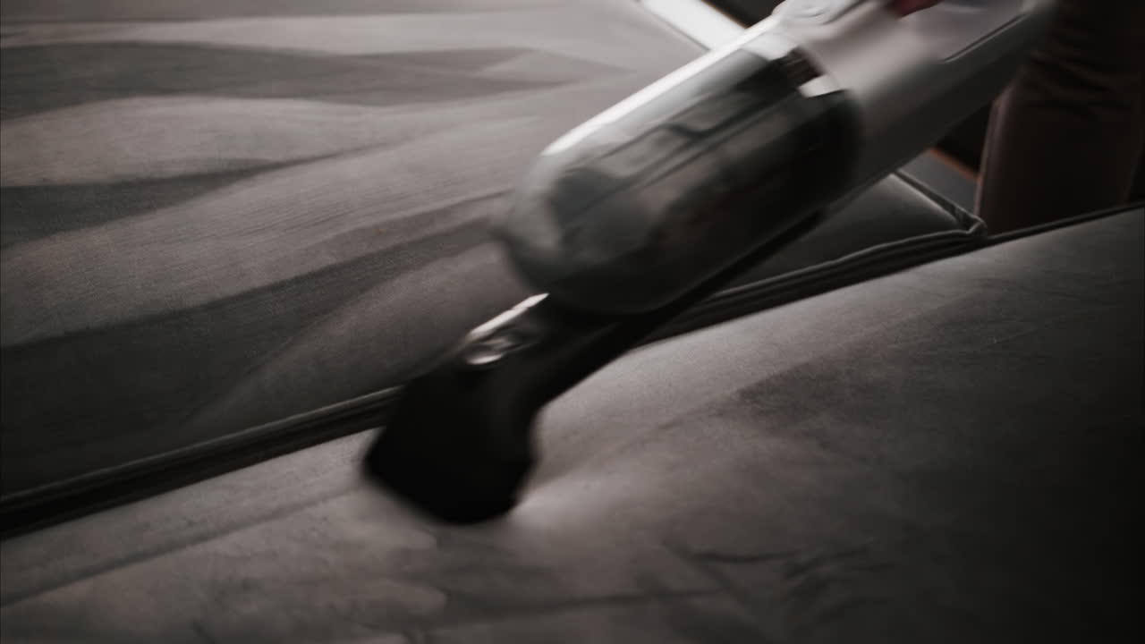 Close up of a woman cleaning a grey couch with a small vacuum cleaner