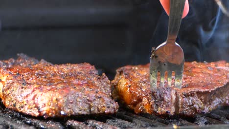 the best shot of a fork turns a nearly cooked juicy rib eye steak on a grill and orange flames shoot up out from underneath it