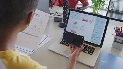 mujer de negocios afroamericana en el escritorio, leyendo un informe, usando una computadora portátil y un teléfono inteligente con espacio para copiar