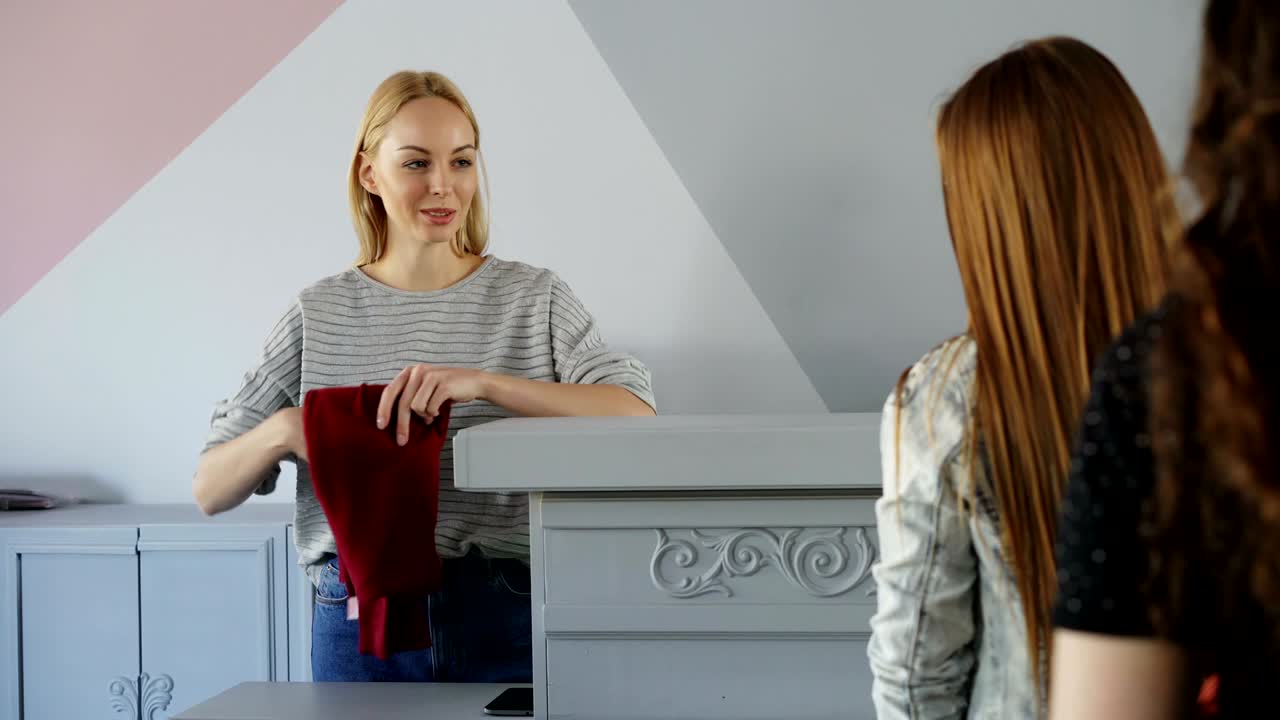 친절한 여성 현금관은 줄을 서 있는 고객에게서 옷을 받아서 지불을 요청하고, 옷을 종이 봉투에 접고 포장하고 구매자에게 주고 있습니다.