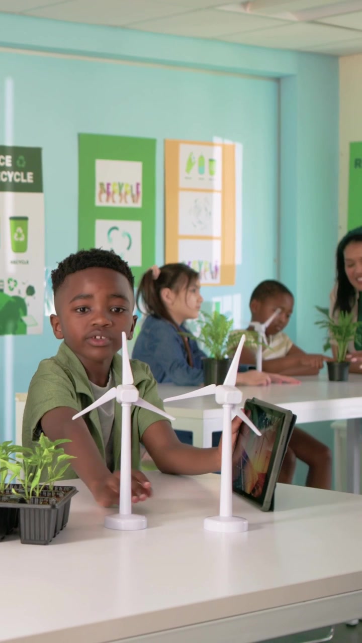 Vertical video: After prompt, boy in green turning wind turbine for science at school with tablet