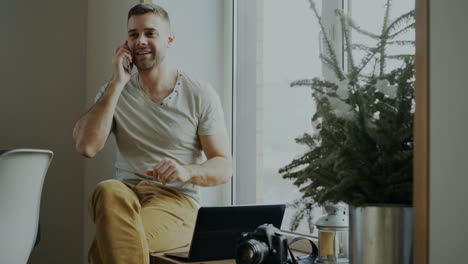 man talking on phone at home, by the window, working