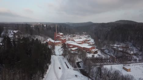 closing in on a big red brick paper mill and factory surrounded by wintery forests and hills and two tall chimney towers