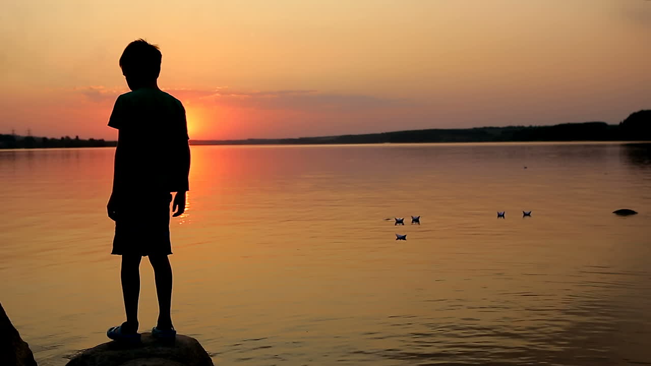 Boy Sending Paper Boat. Boy sitting on stone and playing with paper boat