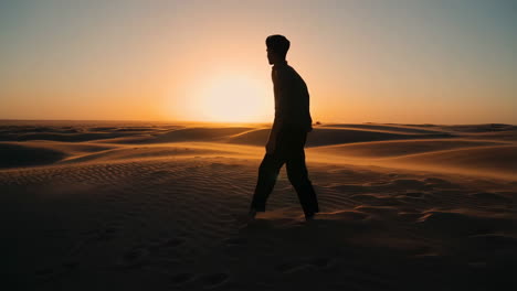 a person's silhouette walking through desert dunes at sunset