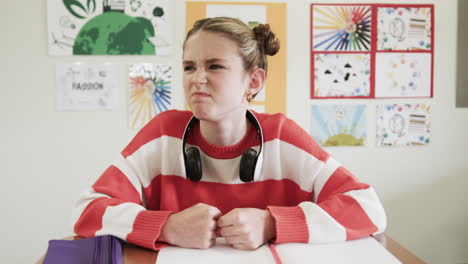 young girl in classroom looking frustrated, wearing headphones, sitting at desk, at school