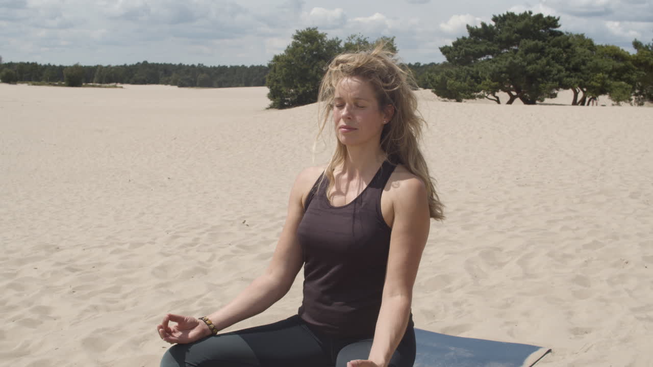 toma estática de hermosa mujer meditando en dunas de arena