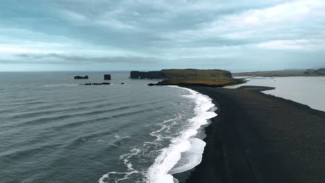 thin line of the beach with black sand among the waters of the ocean. waterfront view with the rock at the back. aerial perspective on the iceland scenery.
