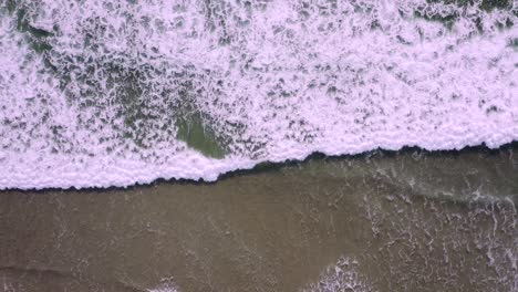 Top down view over foamy water patterns. Ascending aerial reveals powerful swells crashing on golden sand beach. Oregon Coast, Pacific Northwest.