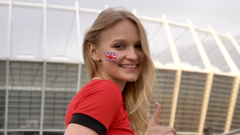 young girl of a blonde football fan of england, smiling, showing like sign, championship concept, stadium in the background 50 fps