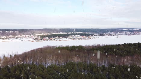 frozen lake and town in horizon in winter season during snowfall, aerial drone view