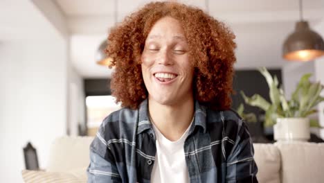 hombre biracial feliz haciendo una videollamada, sentado en el sofá hablando en la sala de estar, cámara lenta