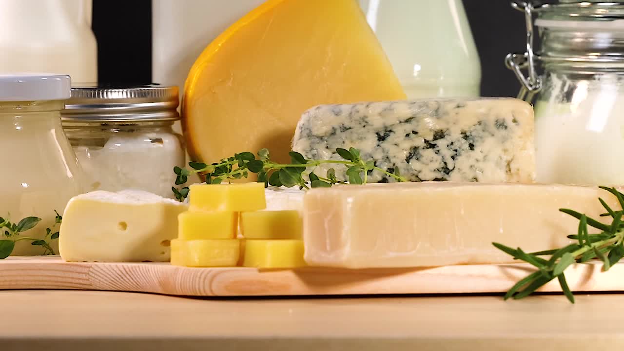 A selection of cheeses and dairy jars arranged with herbs on a wooden board.