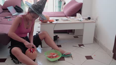 mujer con sombrero de bruja tallando calabaza para halloween