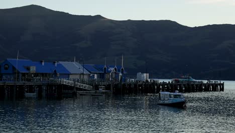 a boat moves towards a pier against a backdrop of mountains during sunset, creating a serene and tranquil scene
