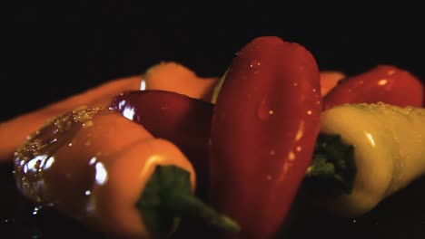 pimientos de plátano coloridos giratorios cubiertos con gotas de agua girando sobre fondo negro e iluminados por luz de estudio
