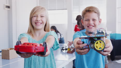 portrait of male and female students holding robot vehicle in after school computer coding class