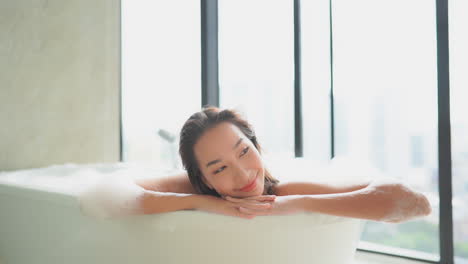 편안한 거품 목욕을 즐기는 만족스러운 아시아 여성