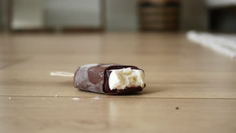 close up of a chocolate covered ice cream popsicle on a wooden floor