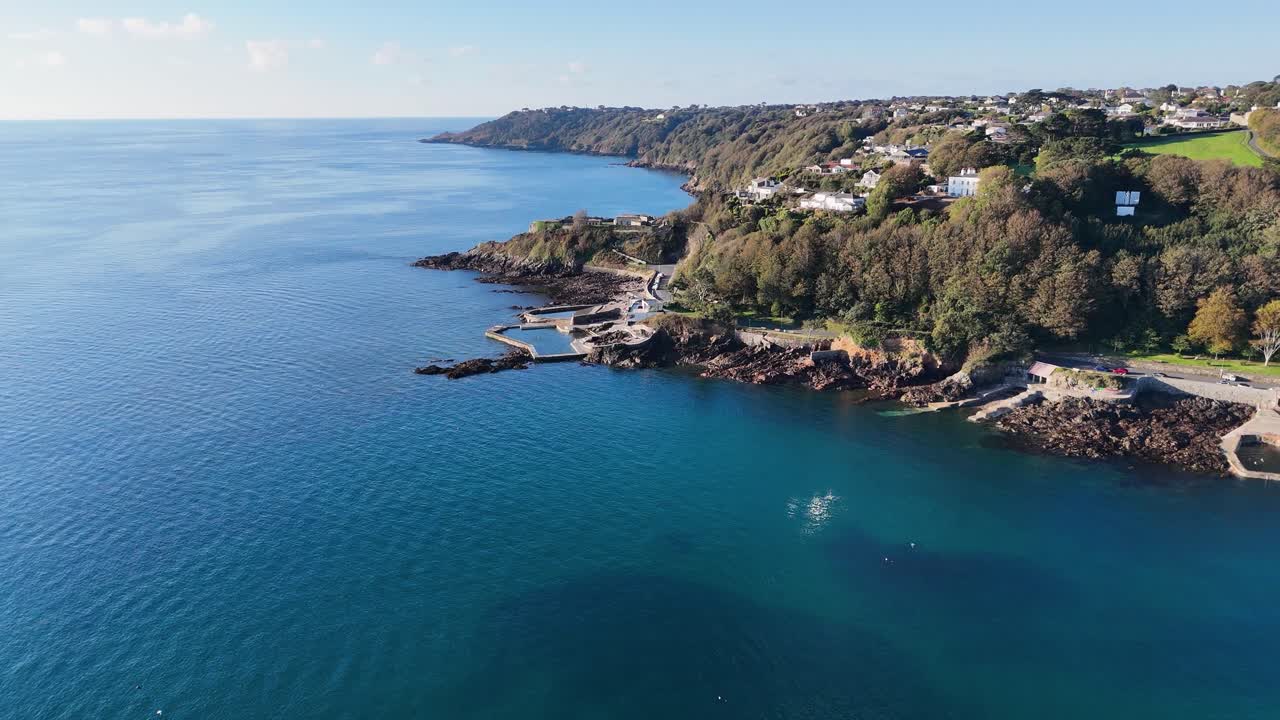 Guernsey high drone flight along eastern coastline showing seawater bathing pools Clarence Battery Fort George and St Martins Point with clear blue calm sea in later afternoon sunshine