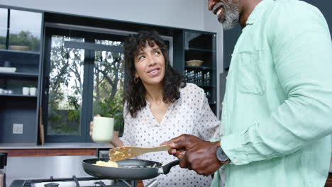 Feliz-Pareja-Birracial-Cocinando-Y-Preparando-Huevos-Revueltos-En-Una-Sartén-En-La-Cocina,-Cámara-Lenta