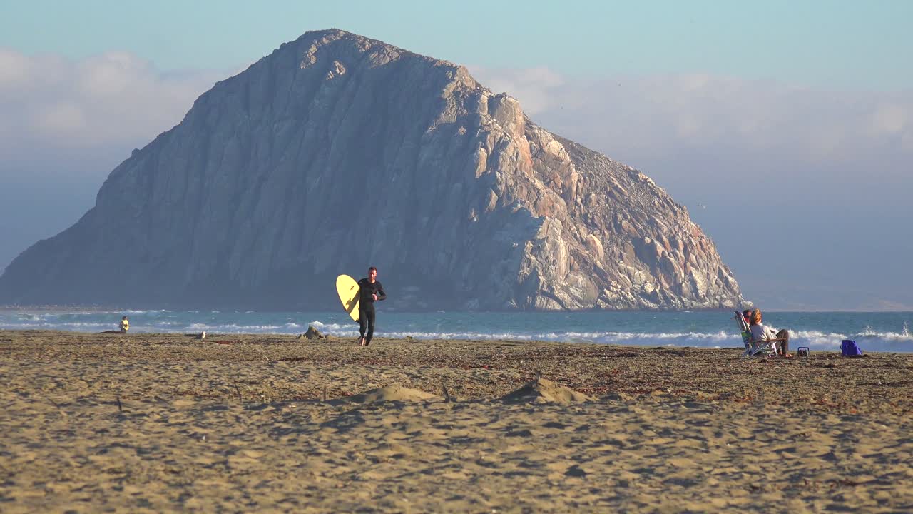 캘리포니아 중앙 해안을 따라 아름다운 모로 베이 바위 앞을 가로지르는 서퍼