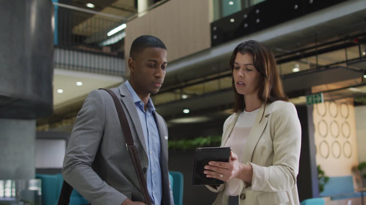 Diverse businessman and businesswoman talking and using tablet in lobby of modern office