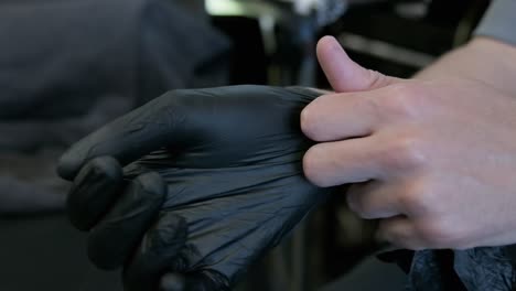 Close up of hands putting on black latex glove full stretch in slow motion.