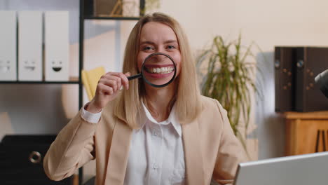 Businesswoman-holding-magnifier-glass-on-teeth,-looking-at-camera,-showing-funny-smiling-silly-face