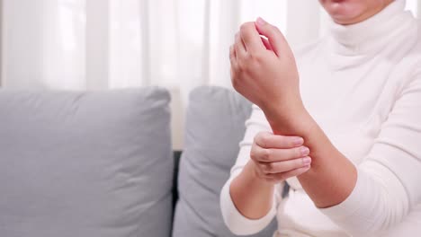 a woman in a white shirt sits on the sofa and massages her arms and wrists