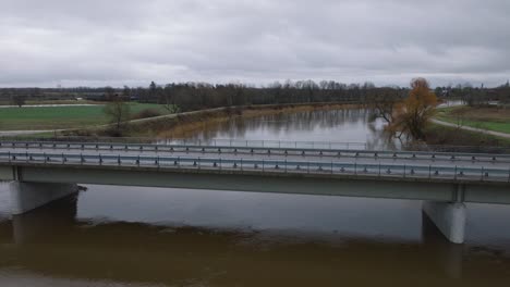 aerial establishing view of high water in springtime, barta river flood, brown and muddy water, overcast day, wide ascending drone shot moving forward over the concrete bridge