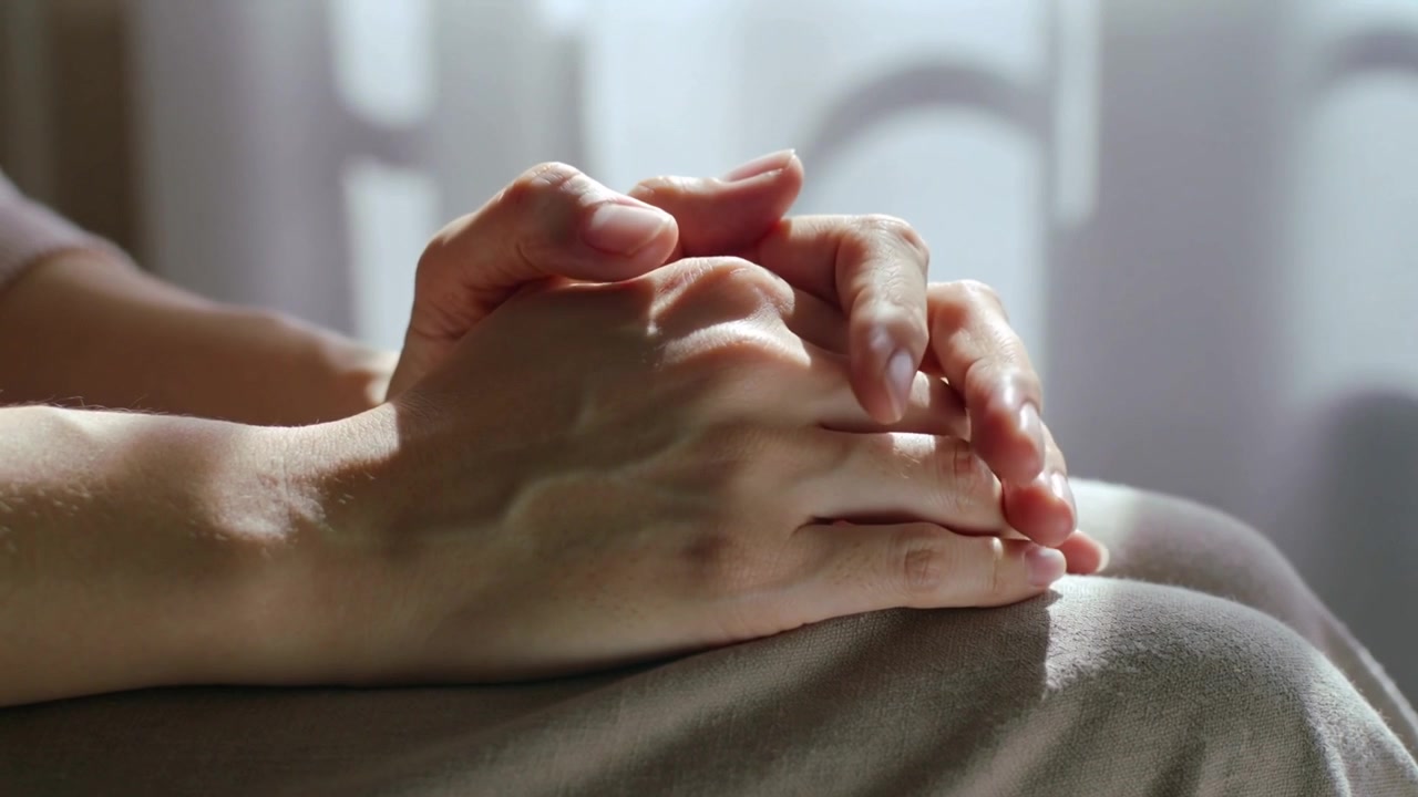 Mani adulte che si muovono, intrecciando e rilasciando le dita su un leggero coprigambe, sistemandosi per comodità.