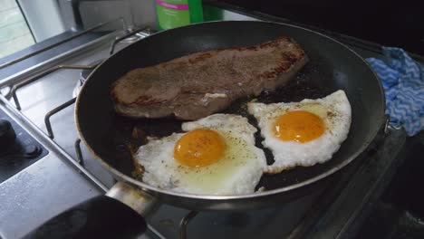 bistec y dos huevos cocinando en una sartén en una cocina de gas en una autocaravana o camper