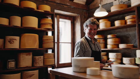 a cheesemonger smiles while cutting a wheel of artisan cheese in a cheese shop