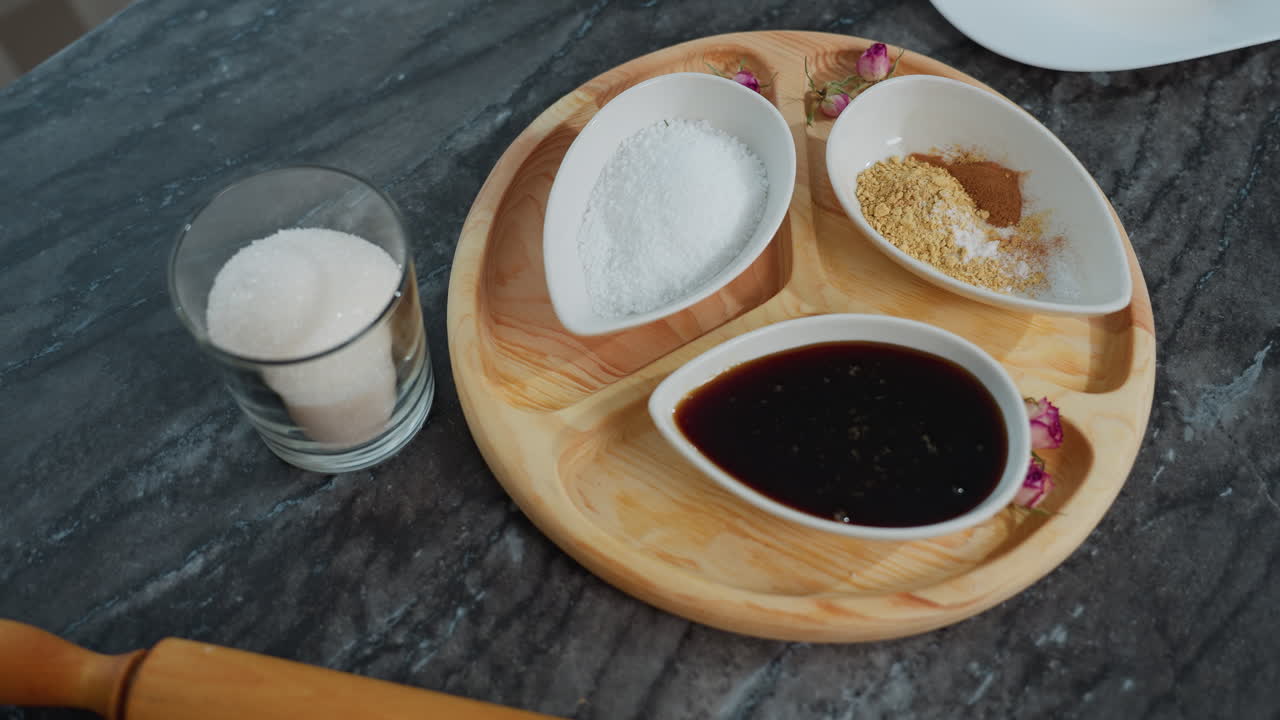 , 향신료, 설탕, 롤링 핀이 있는 나무 트레이를 특징으로 한 검은색 우아한 타일 위의 아침 식사 설정의 오버헤드 뷰, 배경에 부분적으로 보이는 책과 함께 우아한 구성