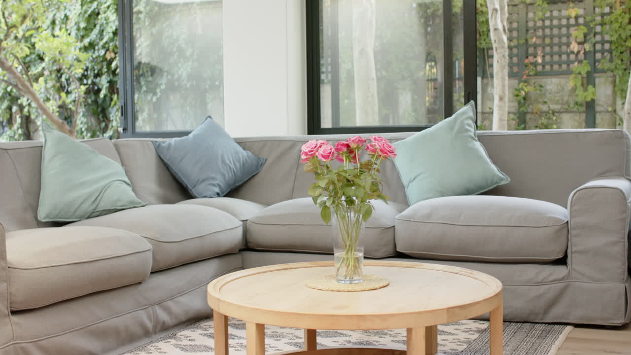 Cozy living room with grey sectional sofa and vase of pink roses on table, copy space