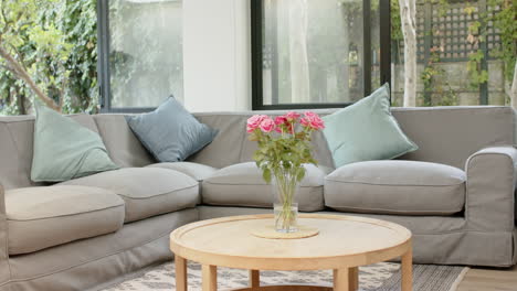 cozy living room with grey sectional sofa and vase of pink roses on table, copy space