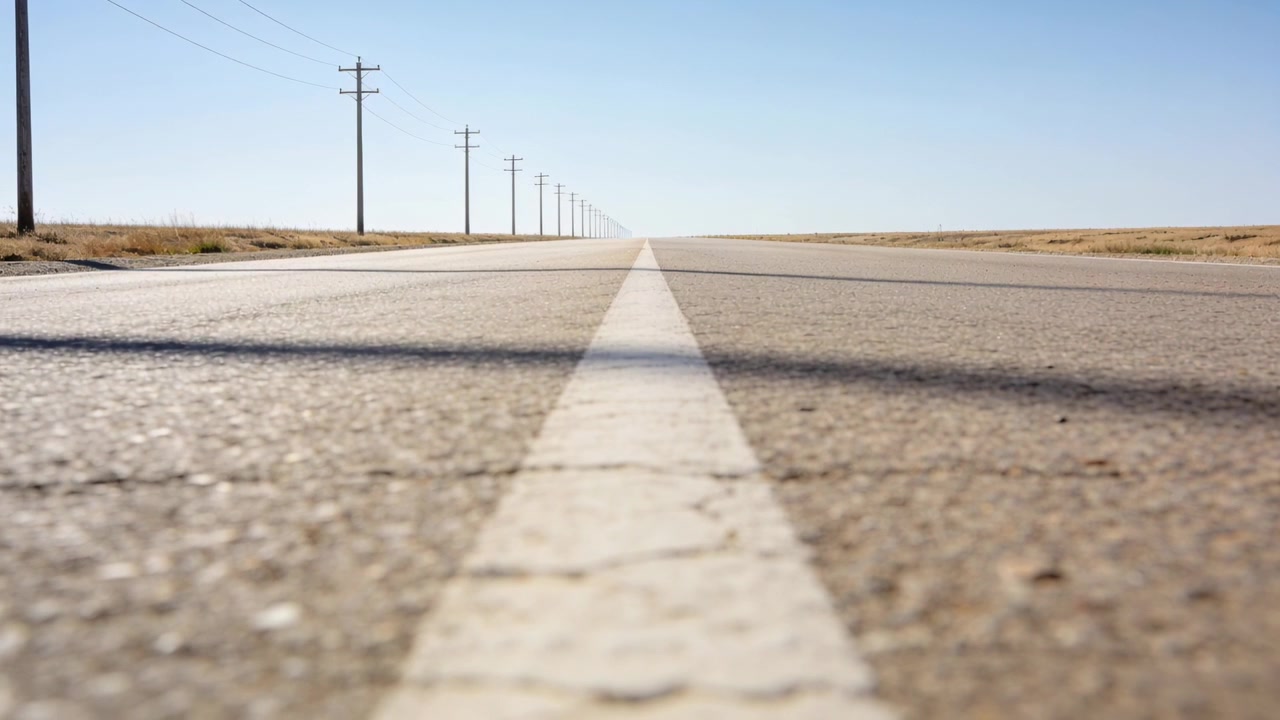 La linea centrale guida l'occhio lungo una strada rurale, con il sole che si sposta, l'ombra che si muove e i pali che si allontanano.