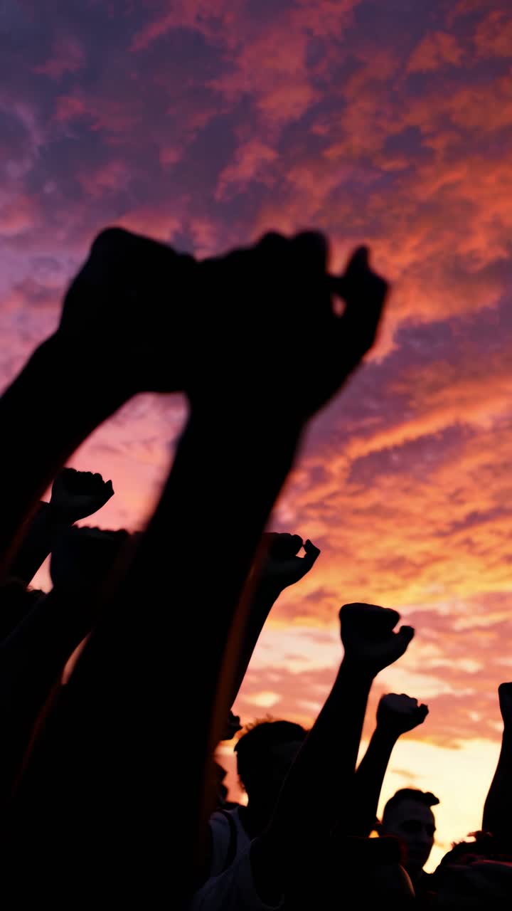 Silhouetted fists raised against a vibrant sunset sky, captured from a low angle