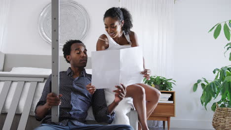 confused man looks at instructions for self assembly baby cot before pregnant wife turns them over