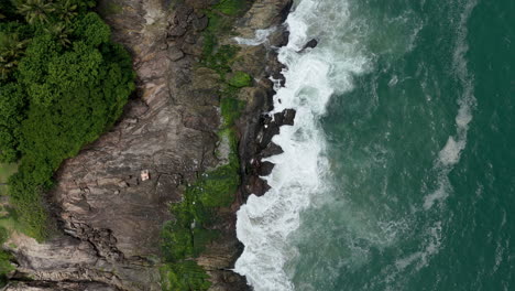 aerial view of waves crashing on a lush green rocky coastline