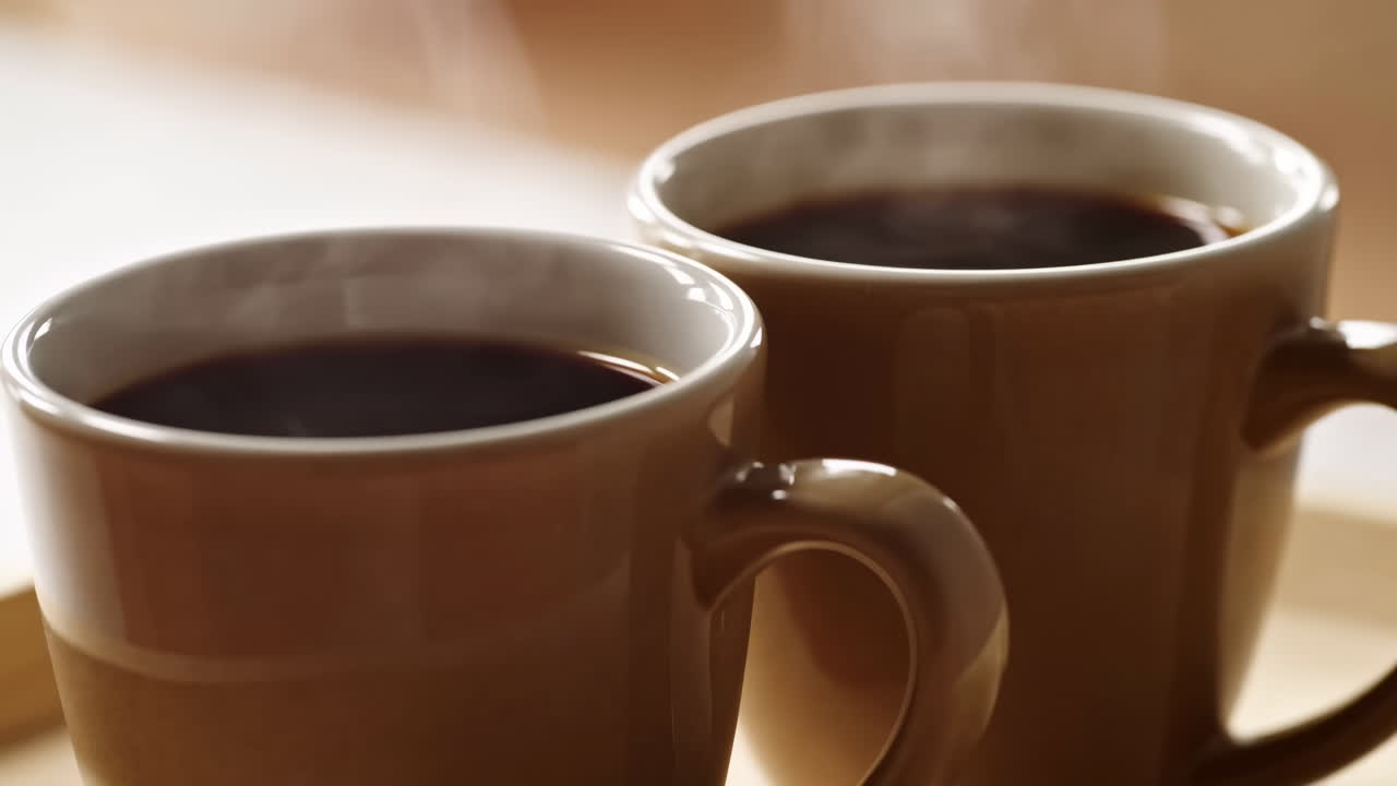 Primo piano di due tazze di caffè fumanti su un tavolo di legno illuminato dal sole, ricca bevanda nera che rilascia vapore delicato, ceramica calda