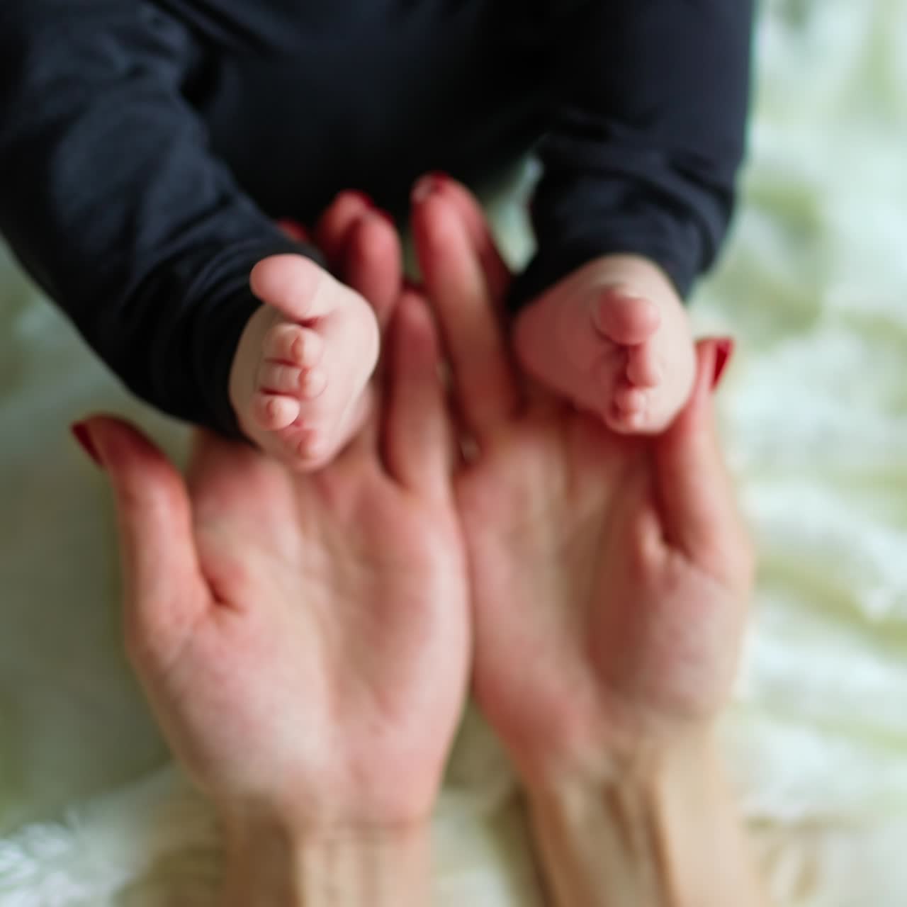 Mom holding little tender baby feet and caressing them. Loving mum's touches of tiny toes of her child. Close up