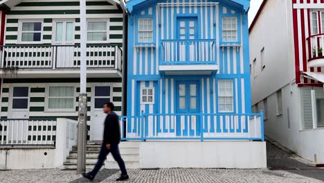 man walking in front of blue stripped house on cobbled footpath, costa nova