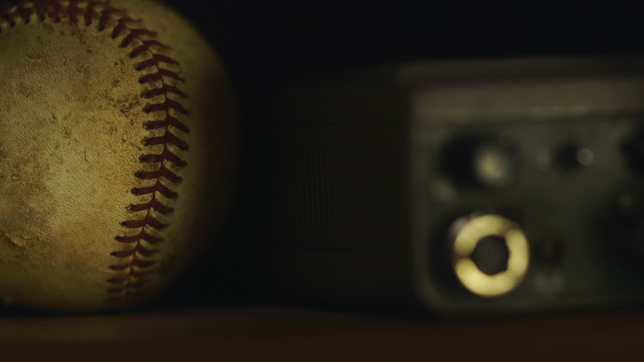 Palla da baseball accanto a dispositivo analogico su scaffale in stanza buia, primo piano.