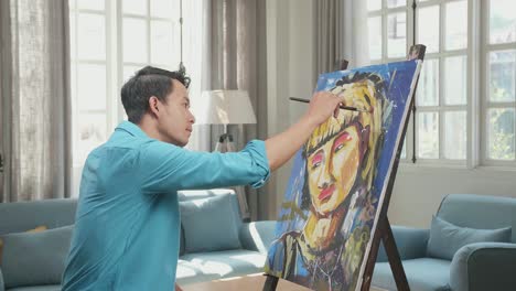 medium shot side view of an asian artist man holding paintbrush mixed colour and thinking before painting a girl's hair on the canvas